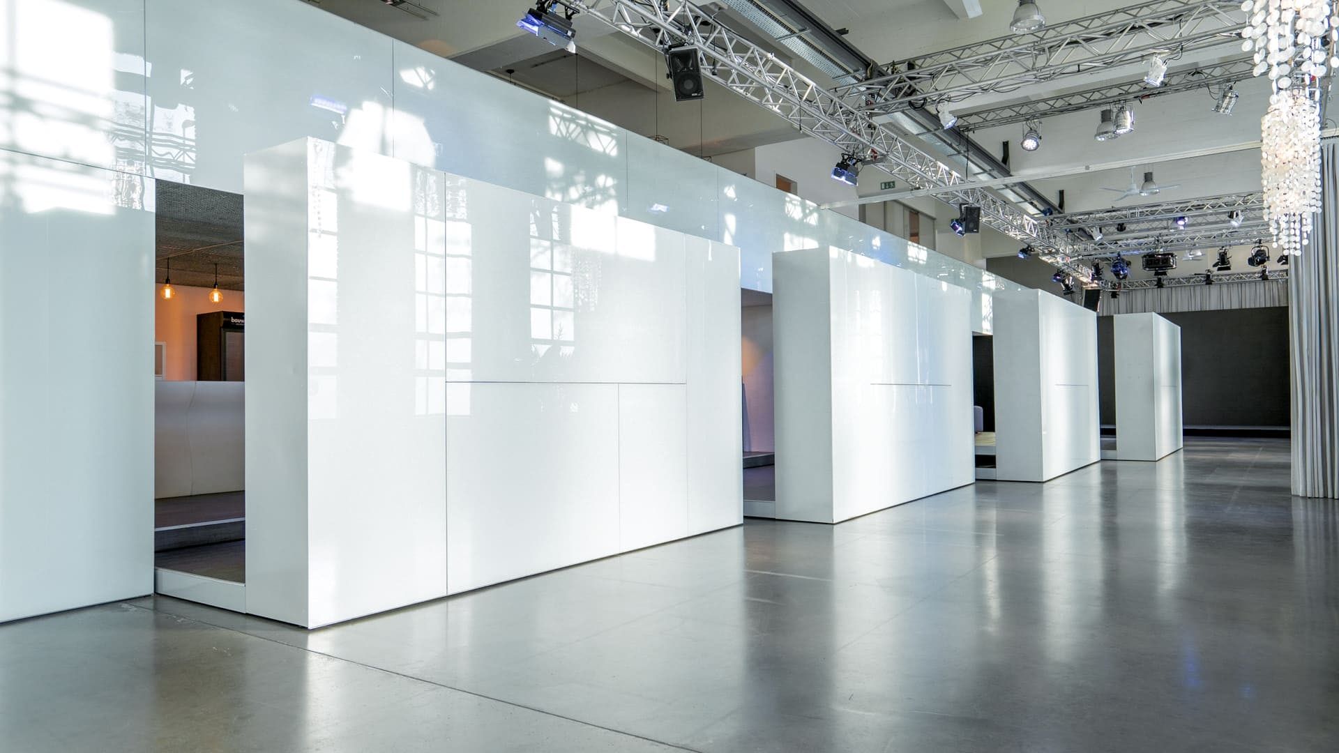 Die leere Halle des Bauwerks in Köln mit weißen Hochglanz-Boxen, Traversen und Tageslicht durch die Industriefenster