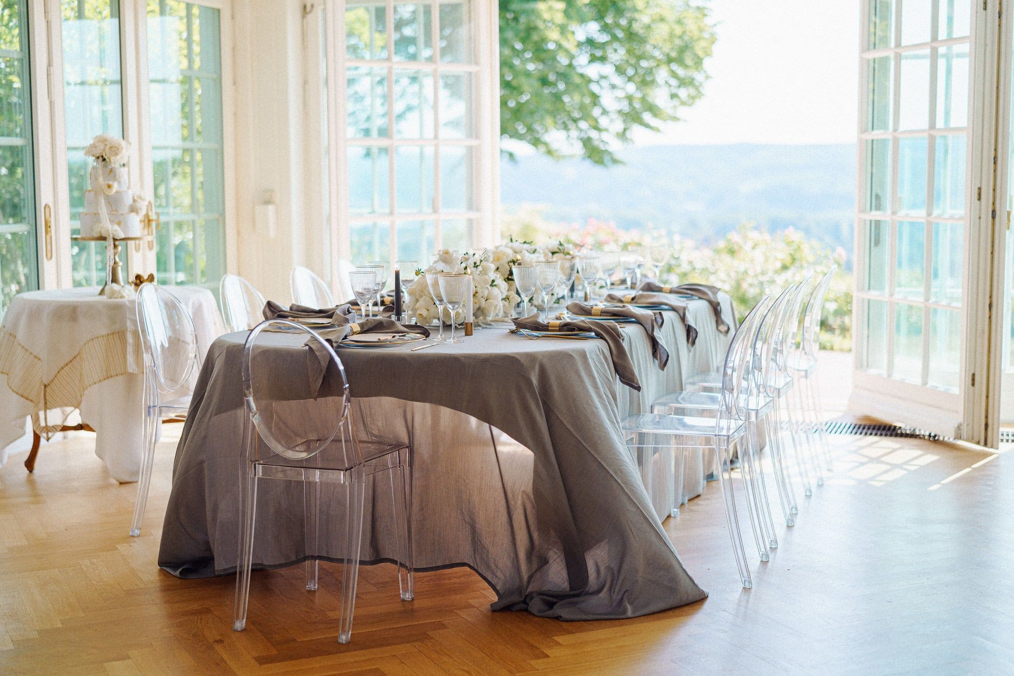 Festlich gedeckte Tafel mit grauen Tischdecken und weißen Blumen in einem Salon der Villa Heckenfels, die Flügeltüren stehen zum Garten offen