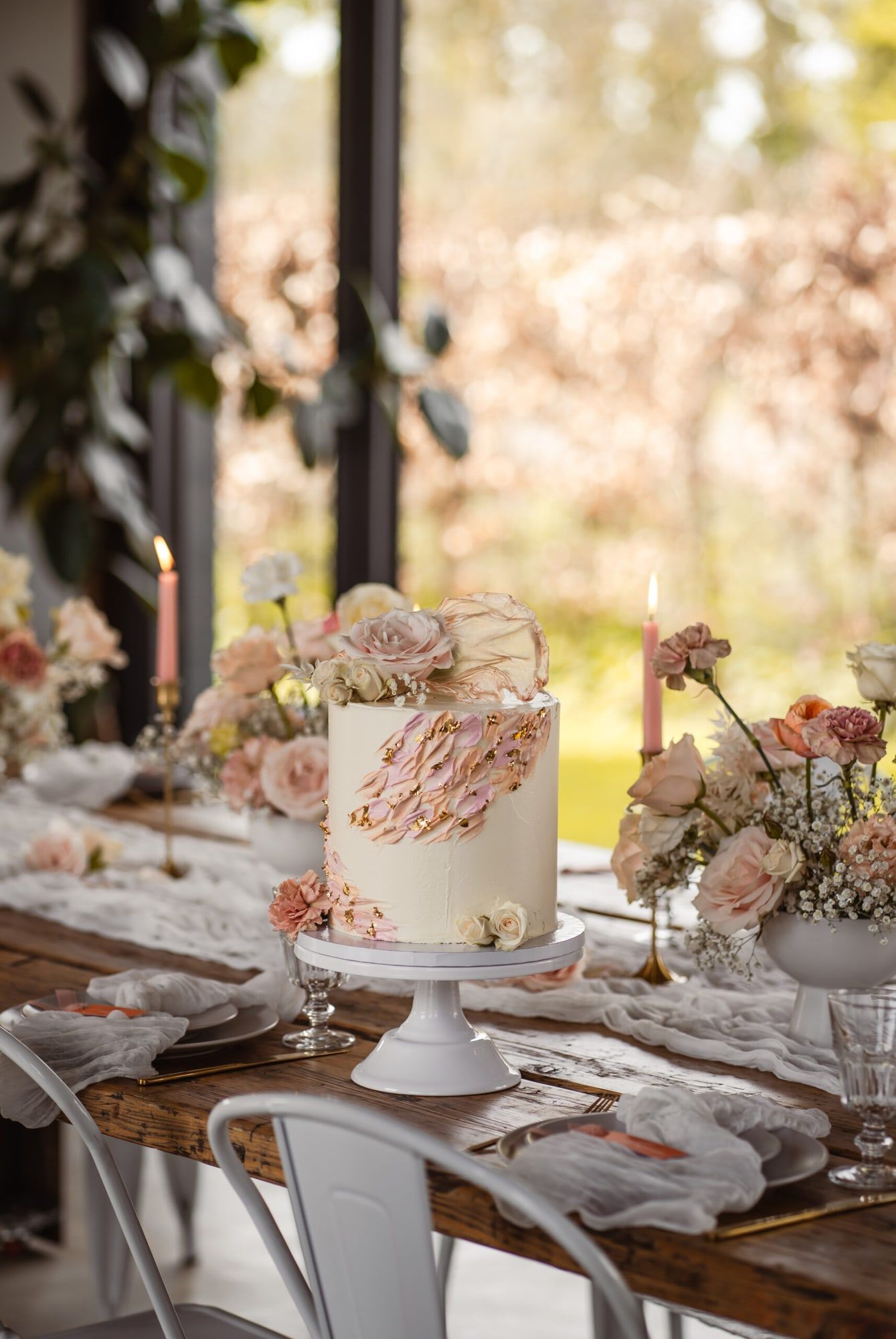Hochzeitstafel mit Holztisch, weißen Stühlen, Blumen und Hochzeitstorte vor den Fenstern des Lofts in Brühl