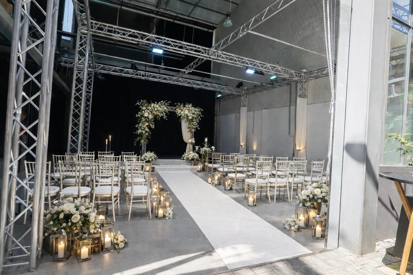 Freie Trauung im Bauwerk Studio Köln, Stuhlreihen am weißen Läufer, Blumenbogen, Laternen und Kerzen, das Tor zum Hof steht offen