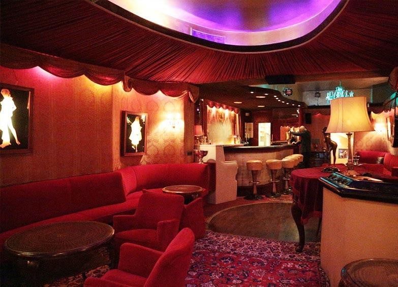 Rote Samtsofas und Sessel unter einer violett leuchtenden Deckenkuppel, im Hintergrund die Theke der Kokett Bar