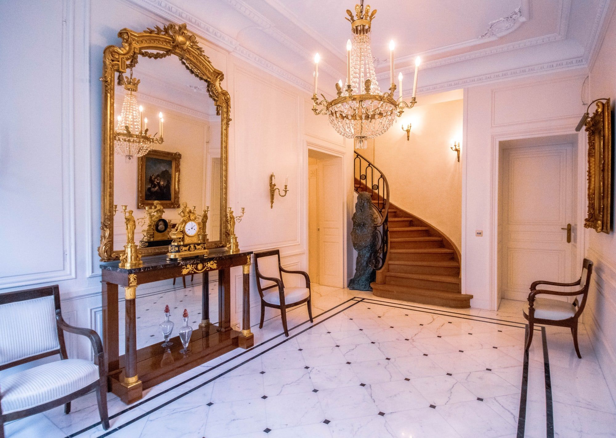 Eingangshalle der Villa Heckenfels mit Marmorboden, vergoldetem Spiegel, Kristalllüster und geschwungener Holztreppe