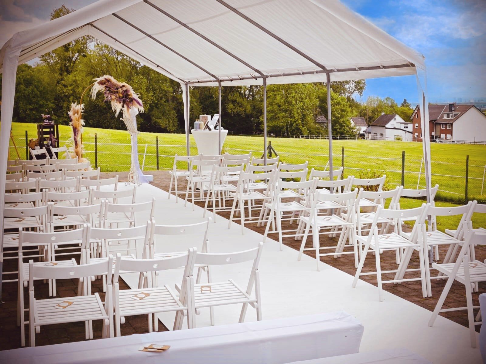 Weiße Klappstühle unter dem Pavillon auf der Festwiese, vorbereitet für eine freie Trauung am Weilerhof