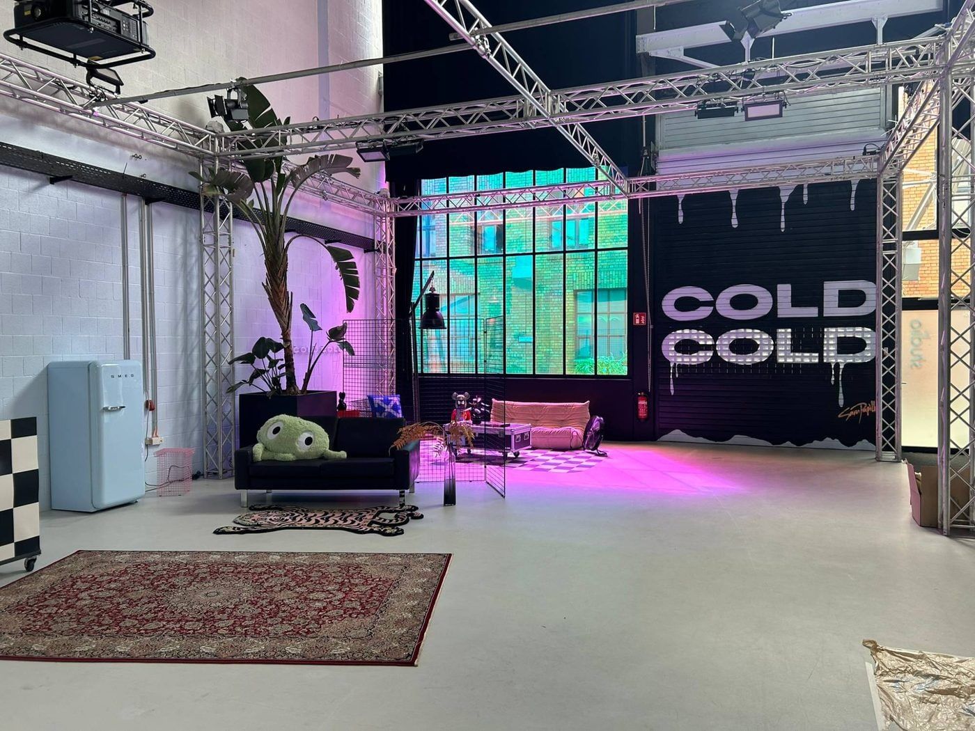 Studiofläche im Bauwerk Köln in pinkem Licht mit Lounge, Palme und hellblauem Retro-Kühlschrank vor Sprossenfenstern