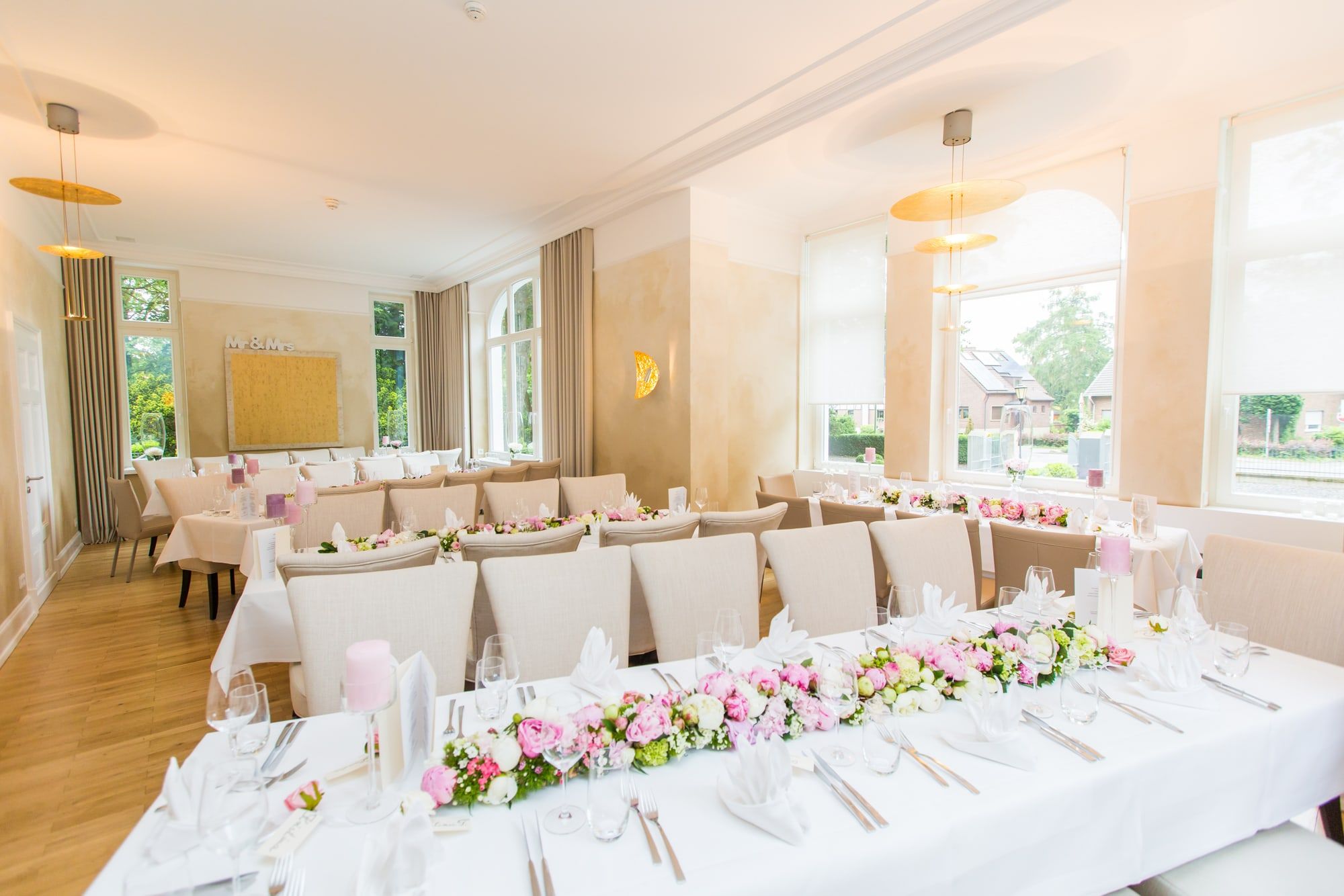 Heller Salon der Villa Andreashaus mit Rundbogenfenstern und einer langen, festlich gedeckten Tafel mit rosa Blumenband