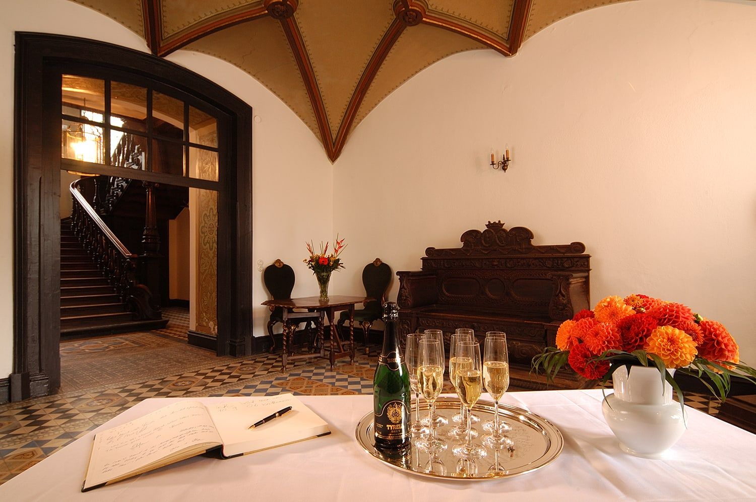 Sektempfang im Entree von Schloss Wachendorf mit gotischem Gewölbe, Gästebuch, Sektgläsern und Blick auf die Holztreppe