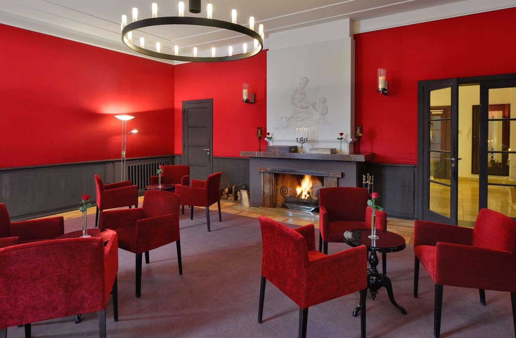 Das Kaminzimmer der Villa Leonhart mit roten Wänden, rotem Sesselkreis und brennendem Feuer im offenen Kamin