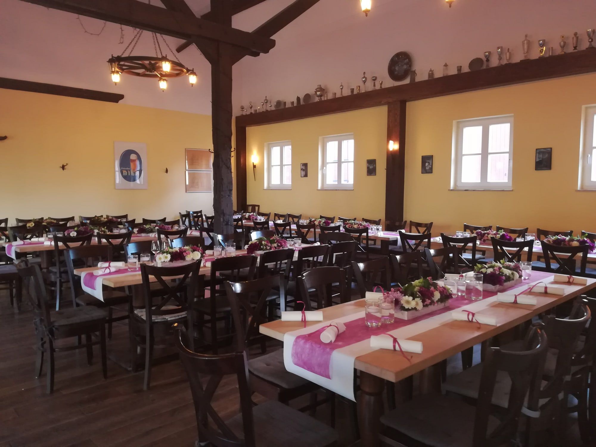Rustikaler Saal mit Holzpfeiler, alten Bierkrügen und Pokalen auf dem Balken und eingedeckten Tafeln