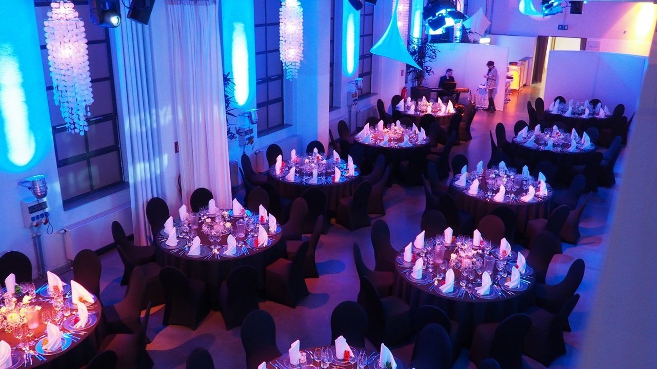 Abendlicher Festsaal im Bauwerk mit runden Tischen, Kerzen und blau-violetter Beleuchtung