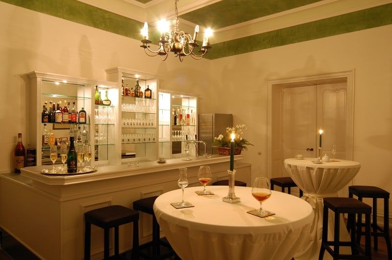 Bar im Grünen Salon von Schloss Wachendorf mit beleuchtetem Regal, Kronleuchter und Stehtischen mit Kerzen