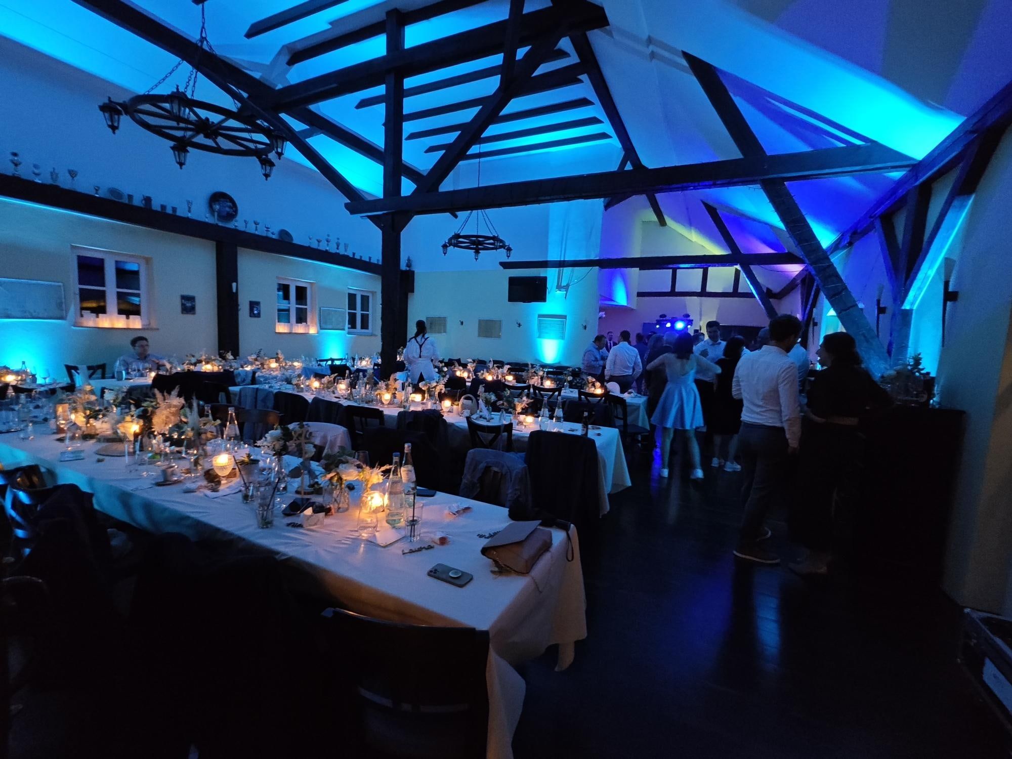 Abendstimmung im Scheunensaal mit blauem Licht, Kerzen auf den Tischen und tanzenden Gästen