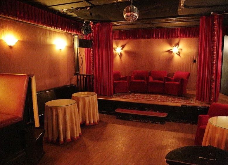 Kleine Bühne im Untergeschoss der Kokett Bar mit roten Samtsesseln, Vorhängen und Sternleuchten an der Wand