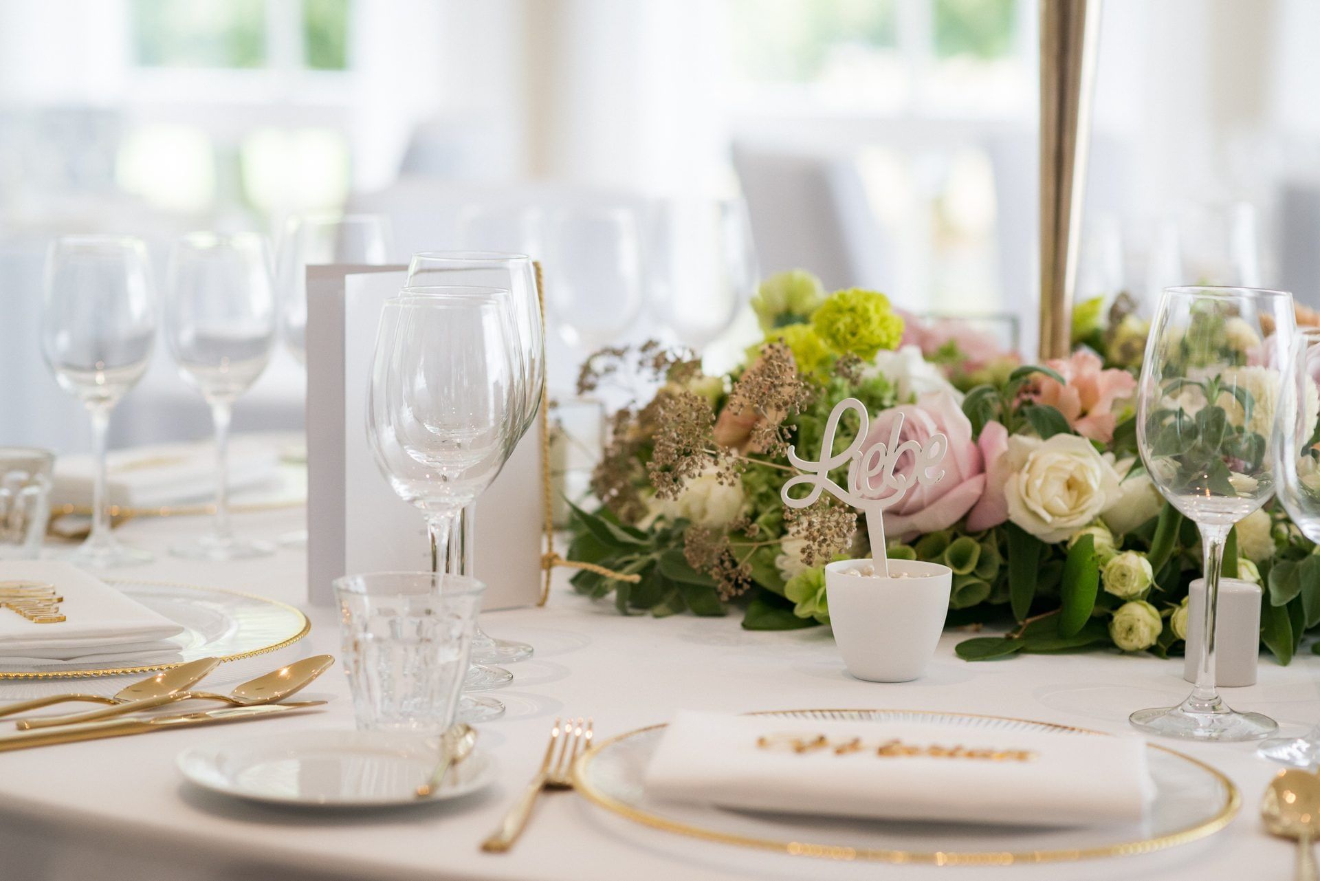 Gedeck mit Goldrand, Namenskarte und Rosengesteck auf einer Hochzeitstafel im Landhaus Velte