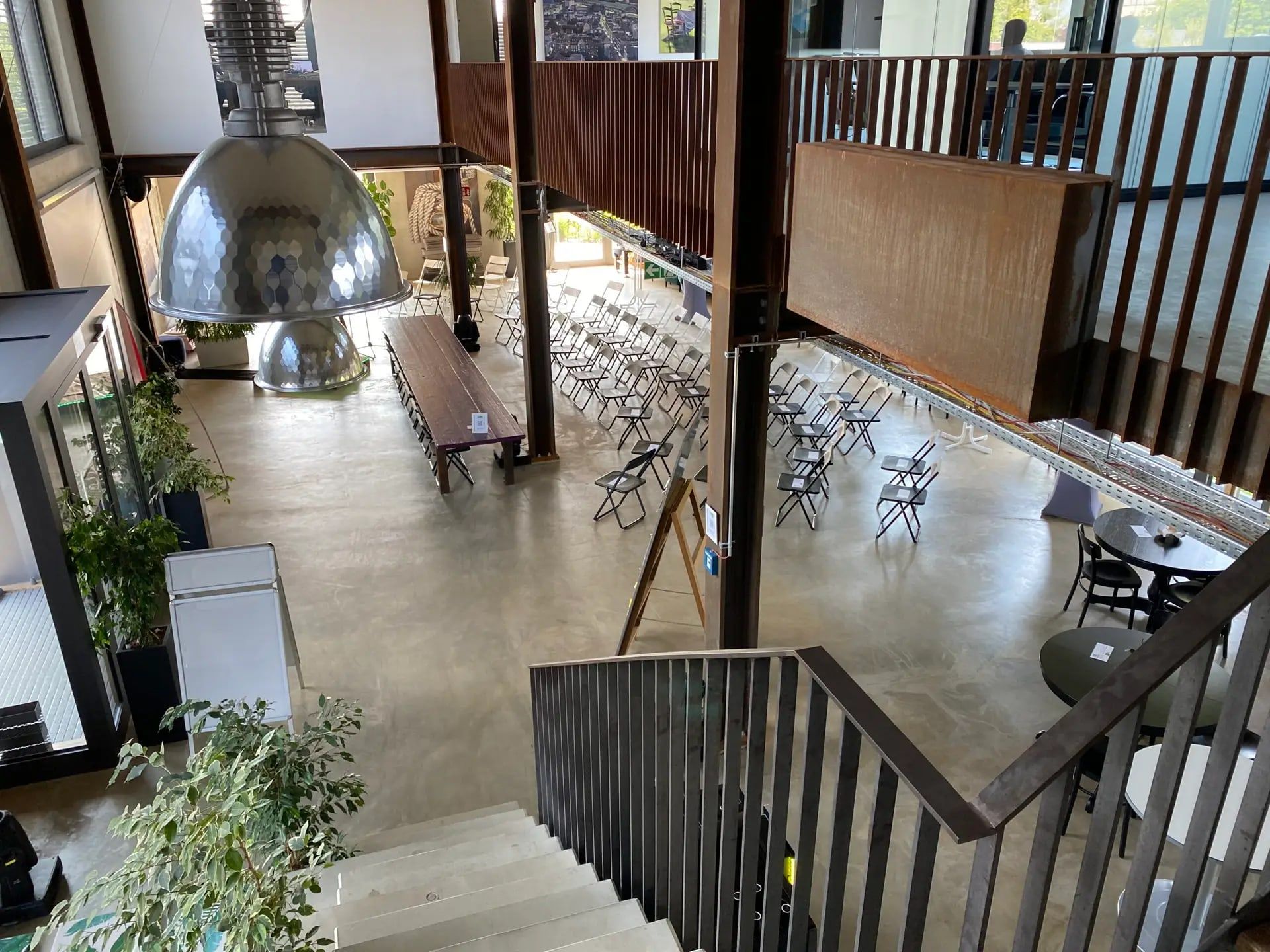 Blick von der Galerietreppe hinunter in den hohen Loft des BRÜNEO mit Industrieleuchte und Stuhlreihen
