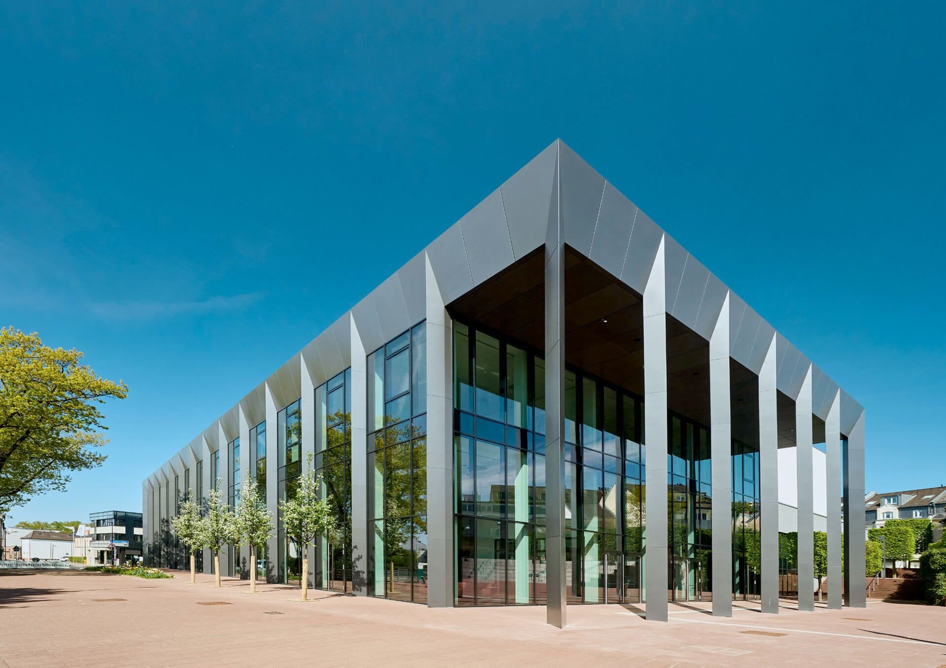 Das Rhein Sieg Forum in Siegburg bei Tag, gläserne Fassade mit Metallpfeilern unter blauem Himmel und Bäumen am Vorplatz