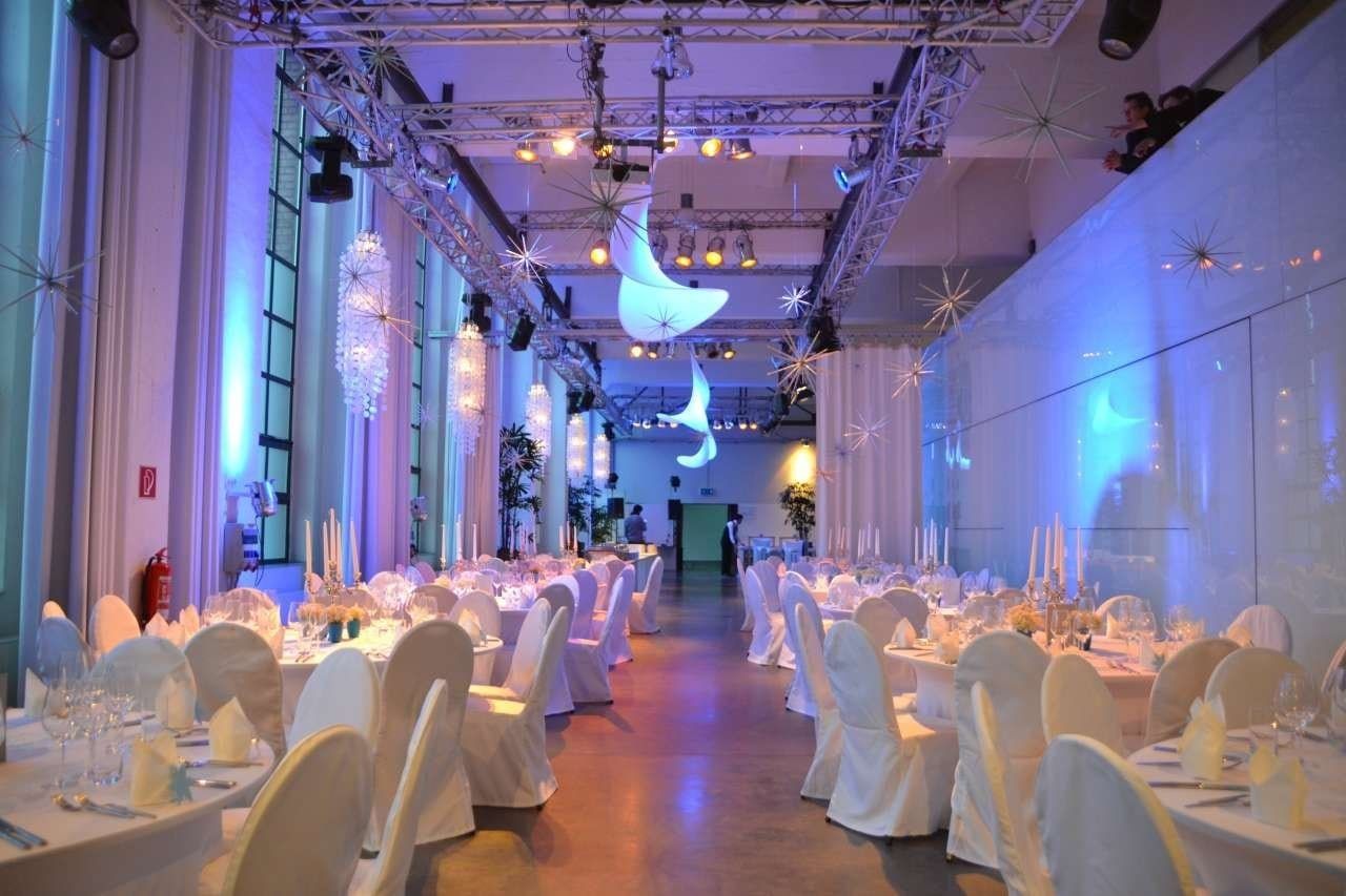 Weihnachtsfeier im Bauwerk, festlich eingedeckte runde Tische unter Sternen und blauem Licht in der langen Halle