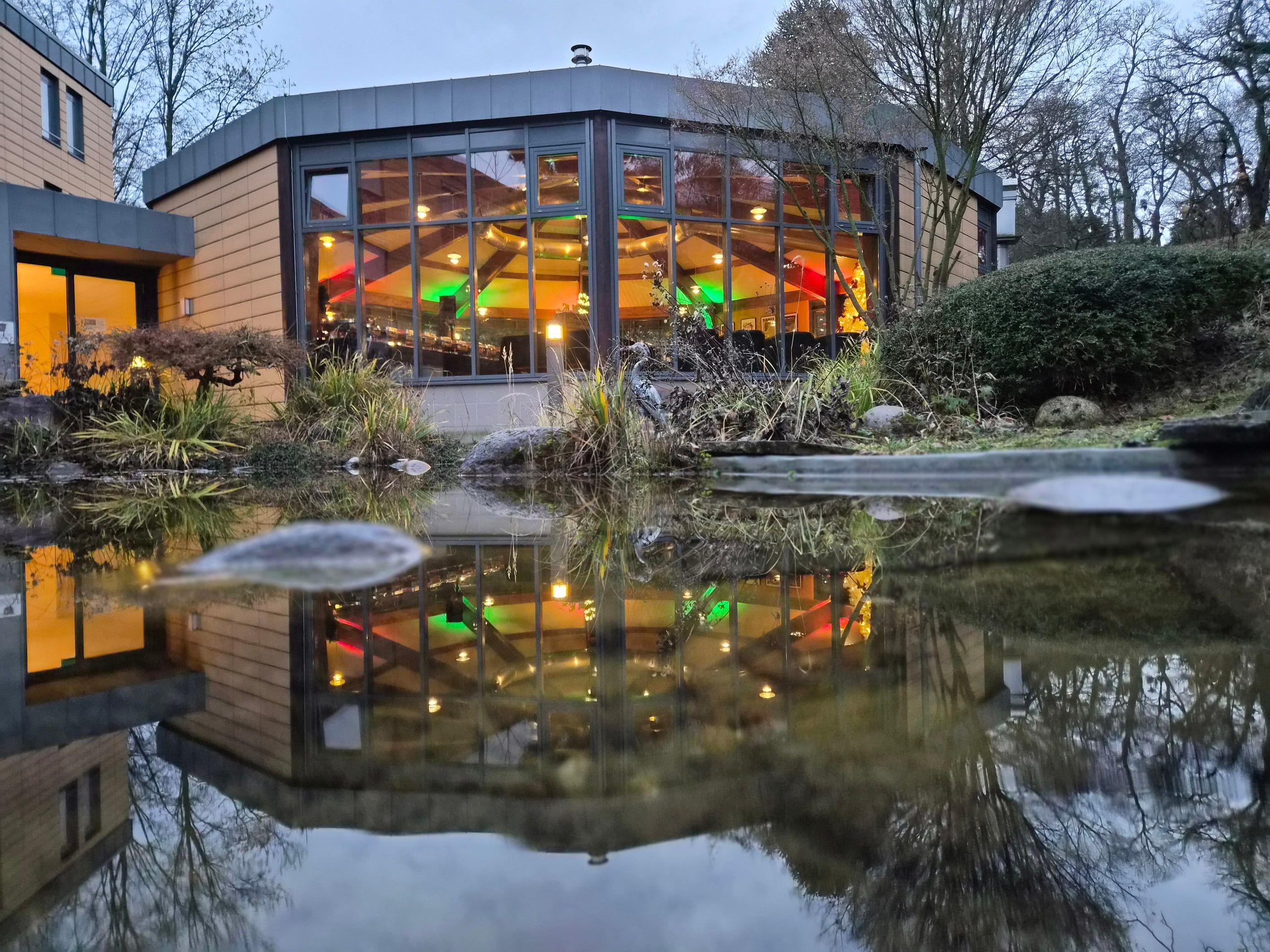 Die Rotunde in Bonn Bad Godesberg in der Dämmerung, der verglaste Rundbau spiegelt sich mit seinen erleuchteten Fenstern im Koi-Teich
