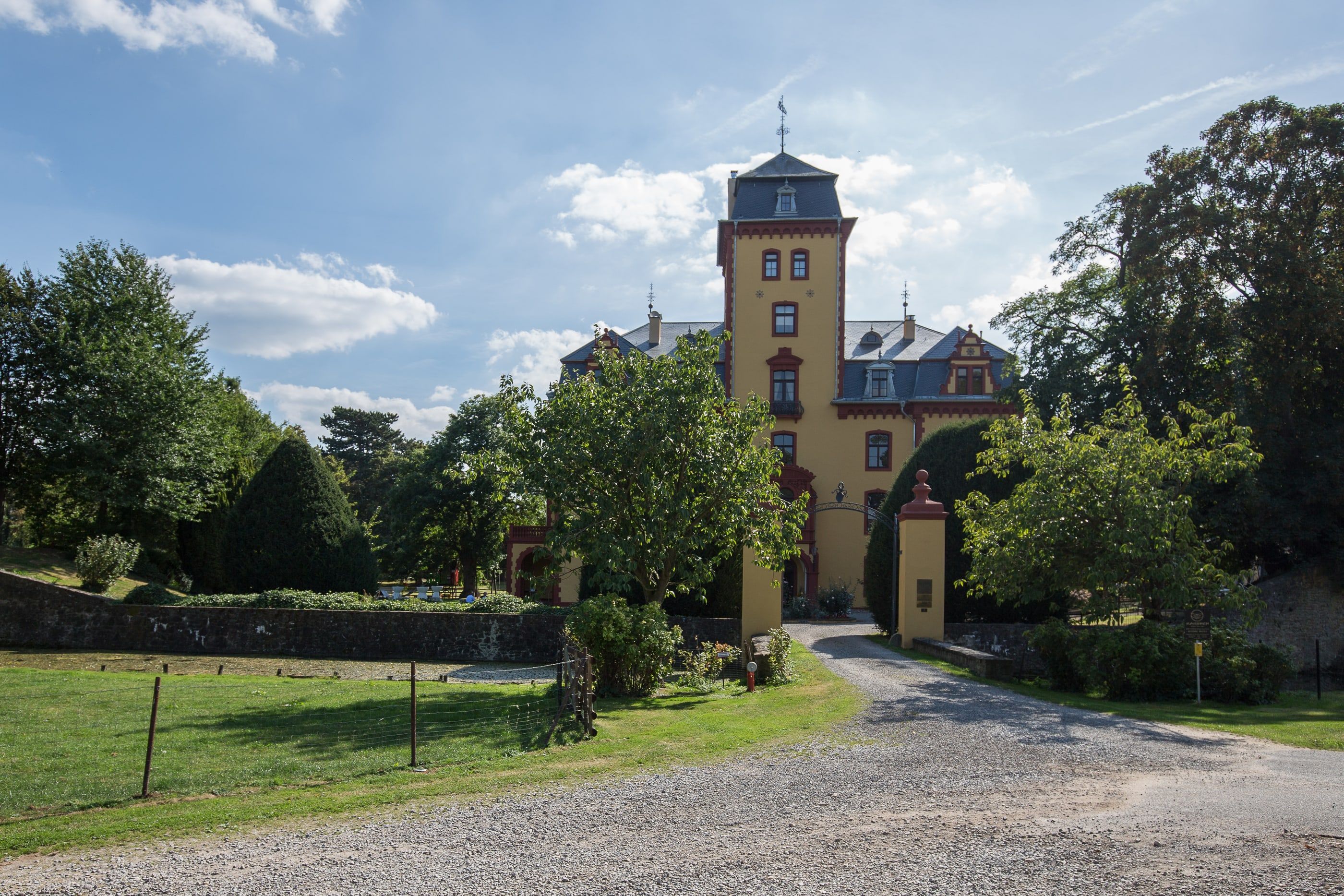 Zufahrt zu Schloss Wachendorf bei Mechernich über die Parkwiese, im Hintergrund das gelbe Schloss mit hohem Turm unter blauem Himmel